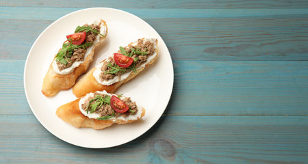 Delicious bruschettas with tuna, cream cheese and tomatoes on light blue wooden table, top view. Space for textの写真素材