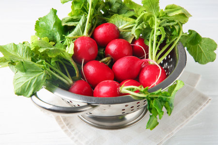 Fresh ripe radishes in colander on white wooden table, closeupの写真素材