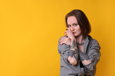 Young woman with piercings, tattoos and stylish clothes posing on yellow background, space for textの写真素材