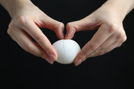 Woman cracking egg on black background, closeupの写真素材
