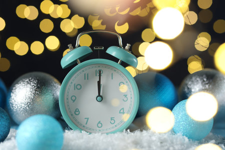 New Year celebration. Alarm clock and festive decor on artificial snow against blurred lights, closeupの写真素材