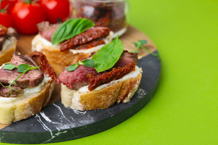 Bruschettas with roast beef, cream cheese, basil, sun-dried tomatoes and fresh vegetables on green background, closeup. Space for textの写真素材
