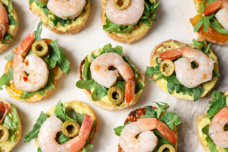 Delicious bruschettas with shrimps, olives and arugula on light table, flat lay