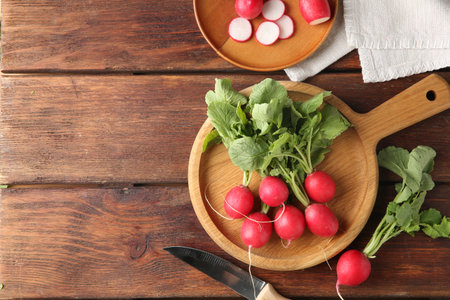 Fresh ripe radishes and knife on wooden table, flat lay. Space for textの写真素材