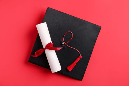 Diploma and graduation hat on red background, top view