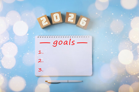 New 2026 Year Goals. Inscription in notebook and cubes with numbers on light blue background, top view. Bokeh lightsの写真素材