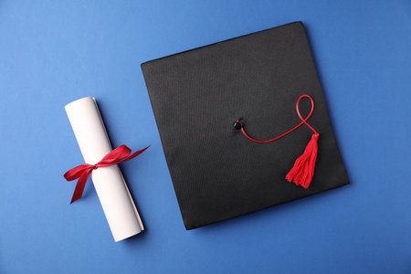 Diploma and graduation hat on blue background, flat layの写真素材