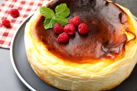 Tasty cheesecake with raspberries and mint on gray textured table, closeup