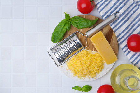 Grated cheese, grater and products on white tiled table, flat lay. Space for textの写真素材