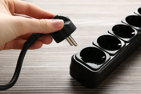 Woman putting plug into power strip at wooden table, closeup
