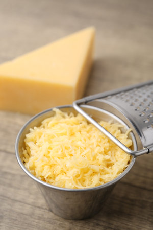 Grated and piece of cheese with grater on wooden table, closeupの写真素材