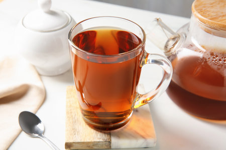 Tasty tea in glass cup, teapot, sugar bowl and teaspoon on white table, closeupの写真素材
