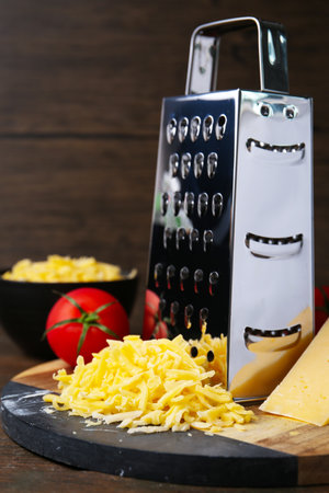 Grated cheese, grater and tomato on wooden table, closeupの写真素材