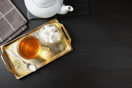 Tasty tea in glass cup, sugar cubes, teaspoon and teapot on black wooden table, flat lay. Space for textの写真素材