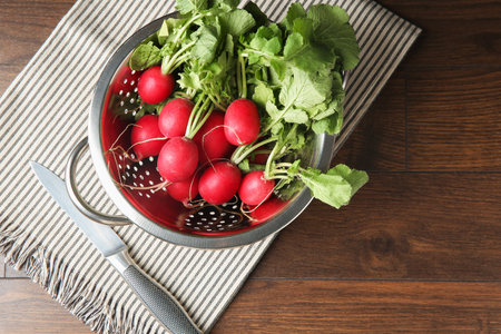 Fresh ripe radishes in colander and knife on wooden table, top viewの写真素材