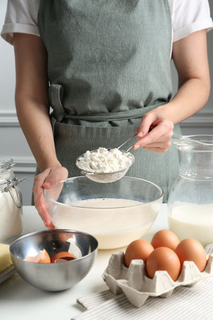Making batter (liquid dough). Woman sieving flour into bowl at white table indoors, closeupの写真素材