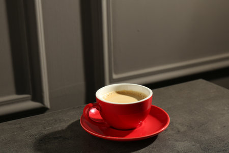 Red cup of aromatic coffee and saucer on dark textured tableの写真素材