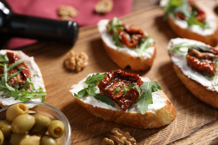 Delicious bruschettas with cream cheese, sun-dried tomatoes, arugula on wooden table, closeupの写真素材