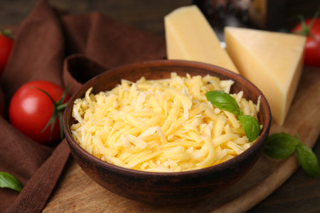 Grated and pieces of cheese with basil on wooden table, closeup