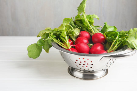 Fresh ripe radishes in colander on white wooden table. Space for textの写真素材