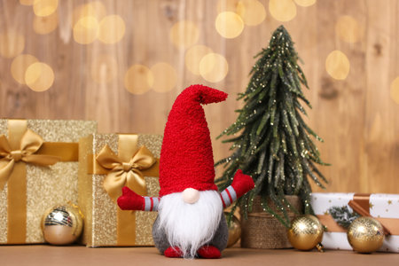 Funny Christmas gnome and festive decor on wooden table against background with blurred lights. Bokeh effectの写真素材
