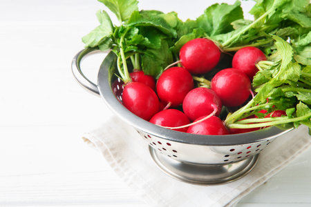 Fresh ripe radishes in colander on white wooden table, closeup. Space for textの写真素材