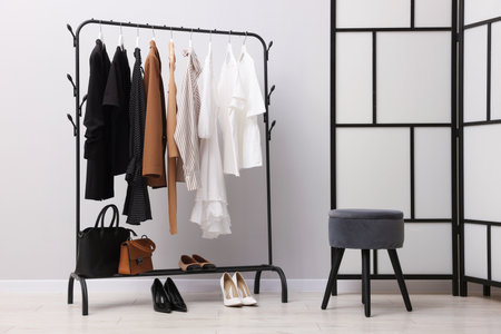 Different stylish clothes hanging on rack, bags and shoes near light wall indoorsの写真素材