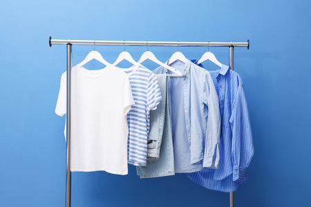Different stylish clothes hanging on rack near blue wall indoorsの写真素材