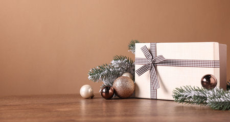 Fir tree branches, gift box and other Christmas decor on wooden table against brown background. Space for textの写真素材