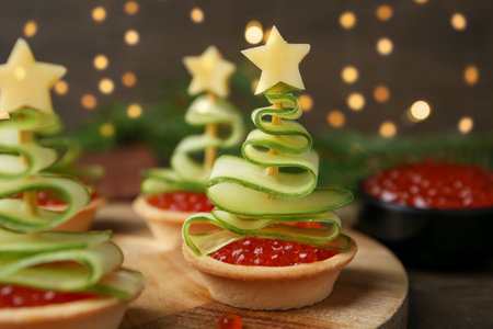 Christmas tree shaped tartlets made with red caviar, cucumber and cheese on wooden table, closeupの写真素材