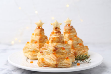 Christmas trees made with puff pastry, red caviar and festive decor on white marble table against background with blurred lights, closeup. Bokeh effectの写真素材