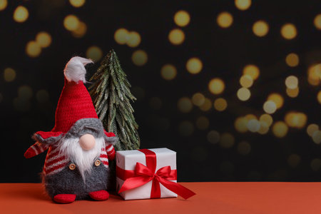 Christmas gnome, fir tree and gift box on color table against dark background with blurred lights, space for text. Bokeh effectの写真素材