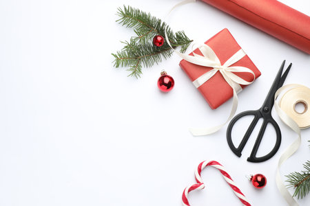 Festive packaging. Gift box, scissors, ribbon, wrapping paper and Christmas decor on white background, flat lay. Space for textの写真素材