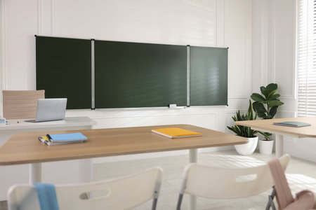 Green chalkboard, backpacks and stylish furniture in classroom. Mockup for designの写真素材