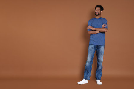 Happy man wearing stylish jeans on brown background, space for textの写真素材