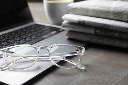 Newspapers, laptop and glasses on gray table, closeup