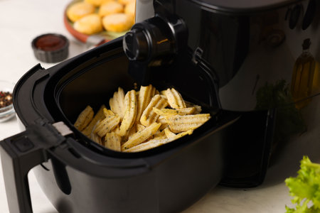 Air fryer with uncooked French fries, chicken nuggets, spices and sauce on white marble table, closeupの写真素材
