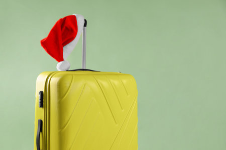 Christmas vacation. Yellow suitcase with Santa hat on olive background, closeup. Space for textの写真素材