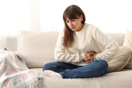 Young woman suffering from stomachache and nausea at homeの写真素材