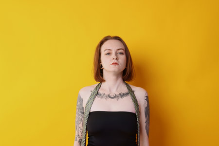 Young woman with piercings, tattoos and stylish clothes posing on yellow backgroundの写真素材