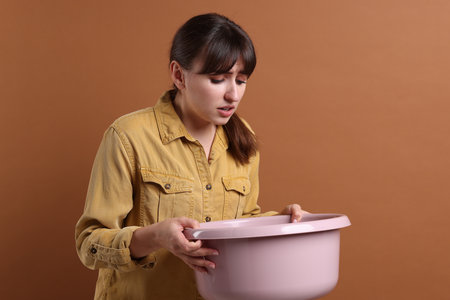 Young woman with basin suffering from nausea on brown backgroundの写真素材