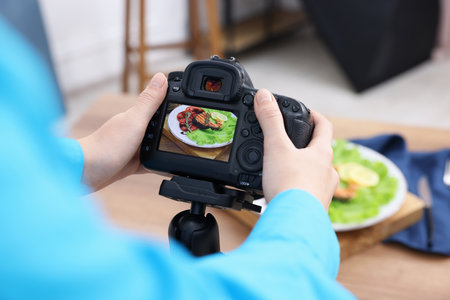Woman taking picture of salmon with vegetables at table in studio, closeup. Professional food photographyの写真素材