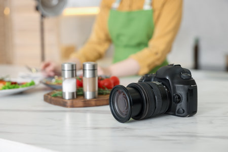 Camera on table and woman creating composition with meal in kitchen, selective focus. Professional food photographyの写真素材