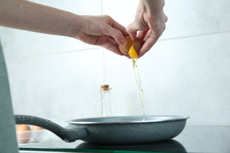 Woman cracking egg into frying pan in kitchen, closeupの写真素材