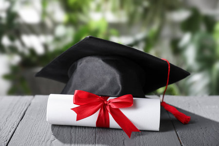 Diploma and graduation hat on gray wooden table outdoors, closeupの写真素材