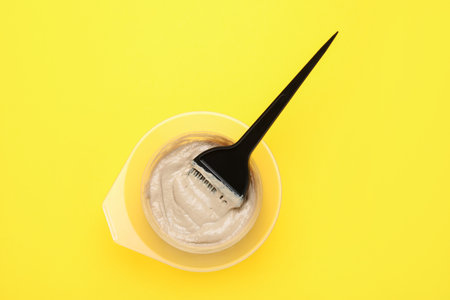 Hair dye and brush in bowl on yellow background, top viewの写真素材