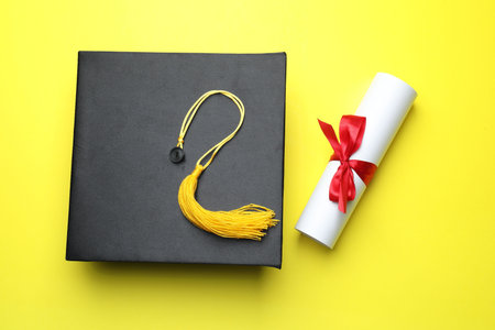 Diploma and graduation hat on yellow background, top viewの写真素材