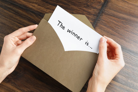 Woman taking card with text The Winner Is from envelope at wooden table, above viewの写真素材