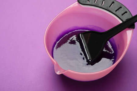 Hair dye and brush in bowl on purple background, closeup. Space for textの写真素材