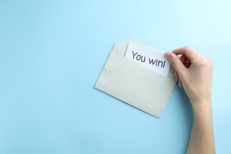 Woman taking card with text You Win! from envelope on light blue background, top view. Space for textの写真素材